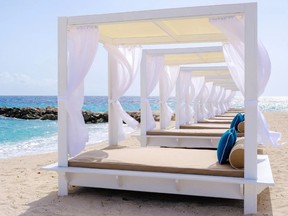 Lounge beds with white covers and curtains on a beach.