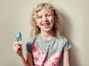 A smiling girl with a missing lower tooth holds a $5 bill.