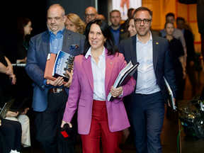 Valérie Plante, flanked by two men, walks into an event holding documents