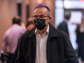 A man with glasses and a mask walks along a hallway.