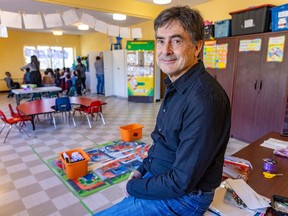 Michael Leclair sits at a table in a community centre, with children in the background