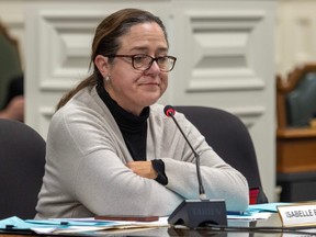 Isabelle Beaulieu sits at a table, arms crossed with a neutral expression, in front of a microphone at a committee hearing