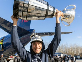 Tyson Philpot hoists the Grey Cup over his head with a plane in the background.