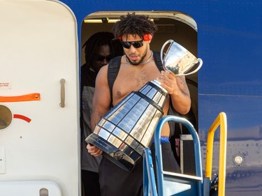 Mustafa Johnson holds the Grey Cup as he leaves a plane
