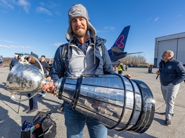 Jason Maas holds the Grey Cup as he walks away from a plane outside