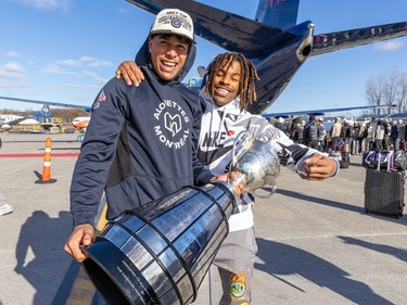 Tyson Philpot holds the Grey Cup and smiles for the camera with James Letcher Jr.'s arm around his shoulder and a plane in the background