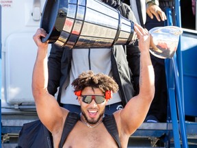Mustafa Johnson holds the Grey Cup over his head on the stairs outside a plane