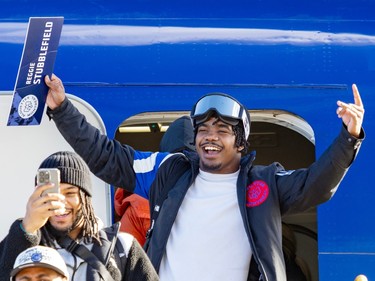 Reggie Stubblefield emerges from a blue plane and raises his arms. In one hand he holds a nameplate with his name on it.