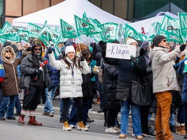 People hold green flags gathered outside on a downtown street, one holds a sign saying 'Utilise ton klaxon'