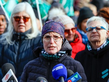 A woman speaks to news media microphones with other people paying attention behind her
