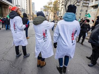 Three people in white lab coats are seen from behind. On the coats is a graphic that reads 'Pas de labos pas d'hopitaux' and the APTS logo