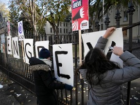Two people put up signs on a fence that read 'En grève'