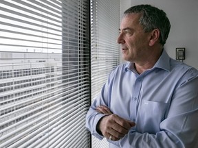 A man looks out a window through blinds.