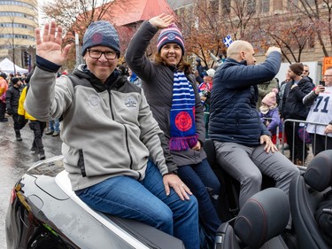 Danny Maciocia and wife Sandra smile and wave at the camera as they sit with Mark Weightman at the back of a convertible car during a parade