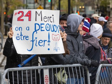 A person behind a crowd control barrier raises a sign that reads '#24 Merci on a Dequoy être fier!' with the Alouettes logo and a fleur de lys