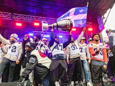 Montreal Alouettes players hold the Grey Cup in the air and wave a Quebec flag on stage