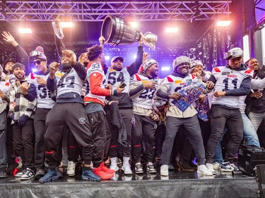 Montreal Alouettes players hold the Grey Cup in the air on stage