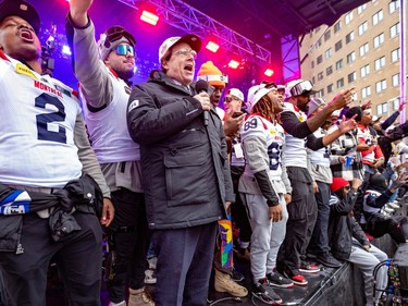 Pierre Karl Péladeau speaks into a microphone on stage surrounded by Alouettes players