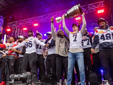 Cody Fajardo raises the Grey Cup above his head on stage surrounded by other Alouettes players