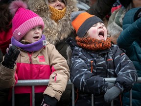 Two children in hats and coats watch a parade.