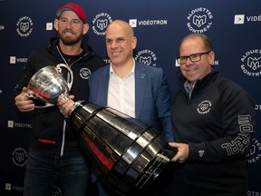 Alouettes president Mark Weightman holds the Grey Cup while being flanked by head coach Jason Maas, left, and GM Danny Maciocia at Olympic Stadium on Wednesday.