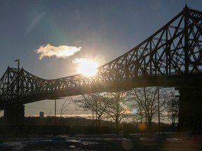 The sun rises behind an iron bridge.