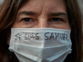 A protestor wears a mask with the slogan 'Je Suis Samuel'