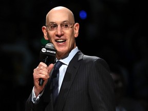 Adam Silver, in a black suit, speaks into a microphone under bright lights