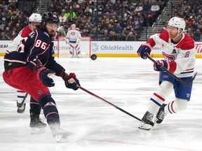 A Blue Jackets and Canadiens player look at a puck in mid-air between them