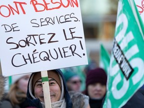 A man holds a sign that says: Ont besoin de services sortez le chéquier!