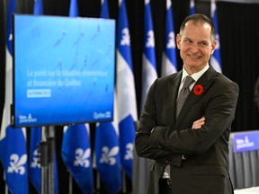 Eric Girard stands with arms crossed and smiling in a room with a large screen and Quebec flags