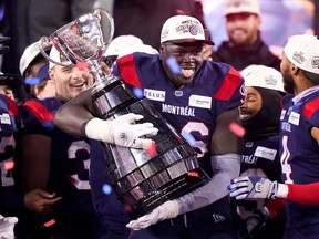 Alouettes defensive-lineman Lwal Uguak grasps the Grey Cup while sticking his tongue out in happiness and surrounded by his teammates.