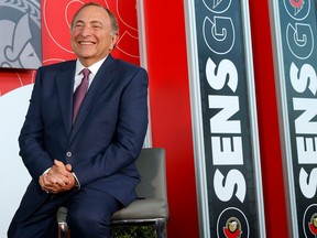 A smiling Gary Bettman is seen sitting next to a "Go Sens Go" poster on the red wall behind him.
