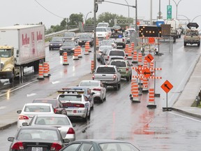 A traffic jam with several cars in a row waiting to get onto an overpass, surrounding by orange traffic cones.