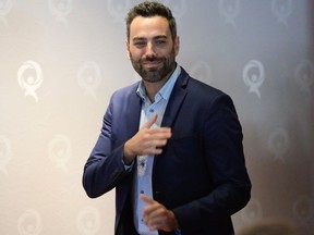 Olivier Bolduc gestures standing in a room with Québec solidaire logos behind him
