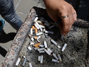 Close-up of a hand putting out a cigarette in a public ashtray filled with stubs.