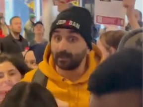 A video still shows a man in a yellow hoodie and black tuque in a crowd