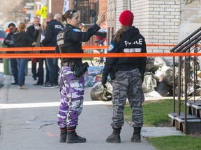 Two police officers wear camouflage pants behind orange police tape