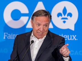 Photo shows Quebec Premier François Legault speaking from a lectern with a blue CAQ sign behind him.