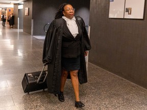 Sharon Sandiford, in courtroom robes, walks down a corridor at the courthouse trailing a rolling briefcase