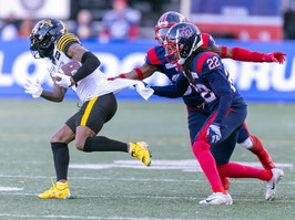 two alouettes players grab the back of the jersey of a tiger-cats player running with the ball