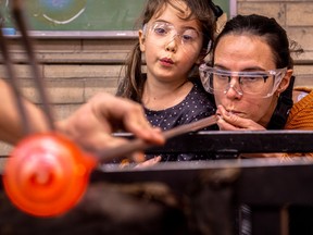 A woman blows through a tube to create a Christmas ornament. Her daughter is standing beside her.