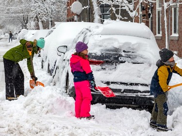 A woman and two children shovel snow around a car parked on a snow-covered street