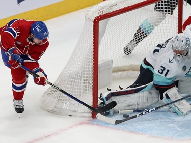 The puck sits below the Kraken goaltender's pad in the crease as a Canadiens player tries to play it from behind the net