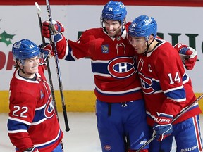 Three Canadiens players embrace while smiling on the ice