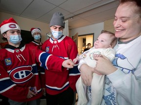 Cole Caufield, wearing a Canadiens jersey and a mask, puts his fist next to the fist of a baby being held up by a woman