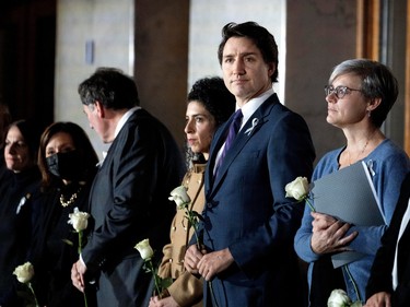 Justin Trudeau looks off to the side while standing between two women, all three holding a white rose