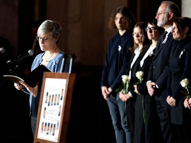 Catherine Bergeron reads into a lectern next to a framed poster of 14 pictures, while others stand behind her holding white roses