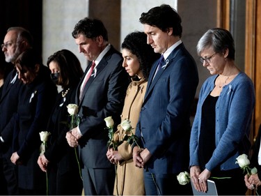 Several people stand holding white roses and bowing their heads