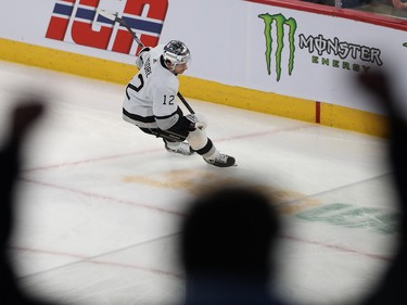 A silhouette of a fan raises two arms in the air in the foreground with a Kings player skating on the ice in the background